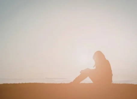 Person sitting by the ocean in soft light, looking out in quiet thought