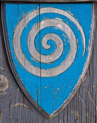 a,wooden,shield,bears,the,spiral,symbol,of,a,whirlpool a,wooden,shield,bears,the,spiral,symbol,of,a,whirlpool