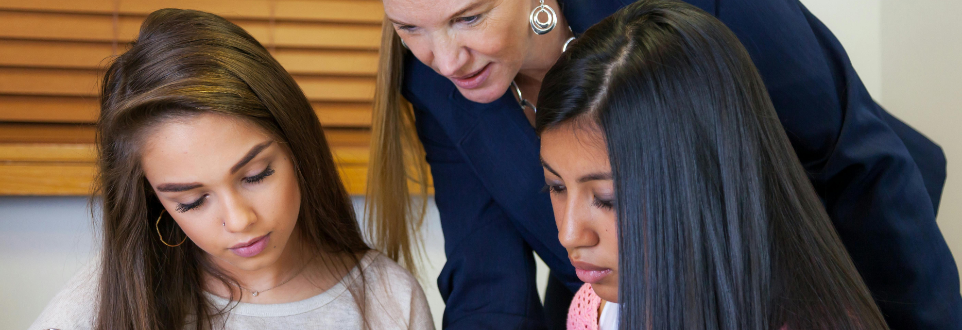 A Teacher Checking In at Eye Level Teacher crouching beside a student's desk to talk quietly, faces not shown